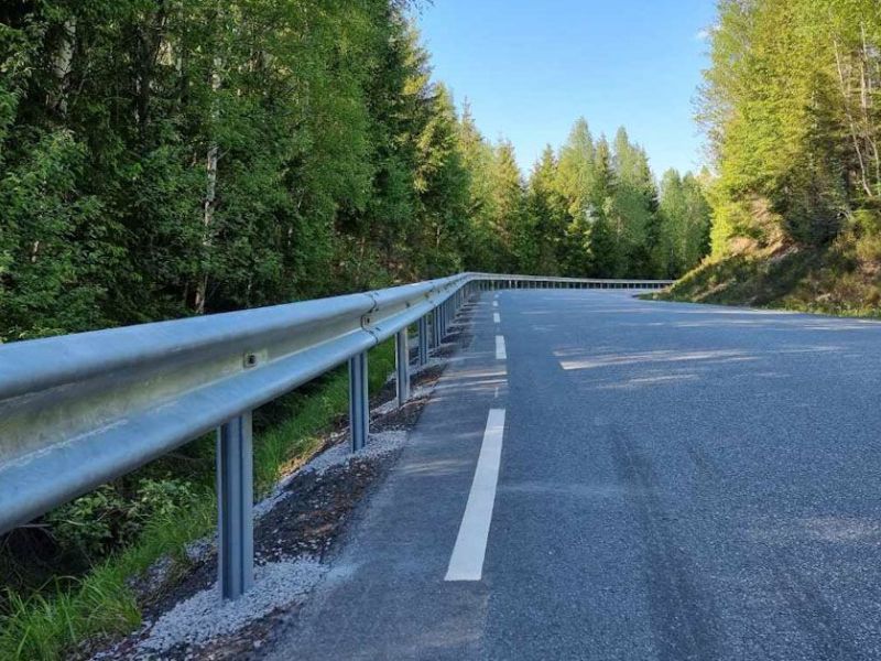 veibane og rekkverk med grønne trær på hver side og blå himmel