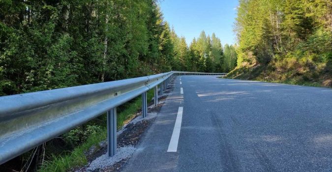 veibane og rekkverk med grønne trær på hver side og blå himmel